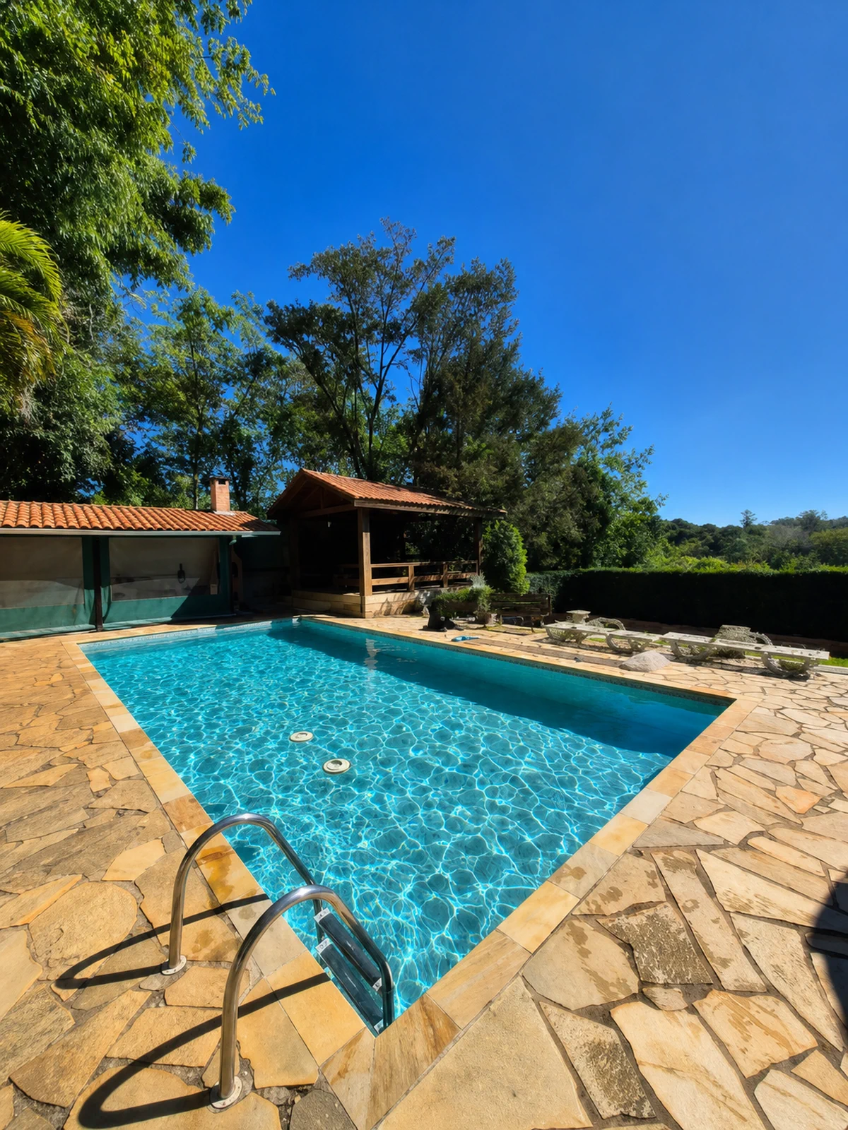Piscina residencial com deck de pedras e água cristalina em Joaquim Egídio